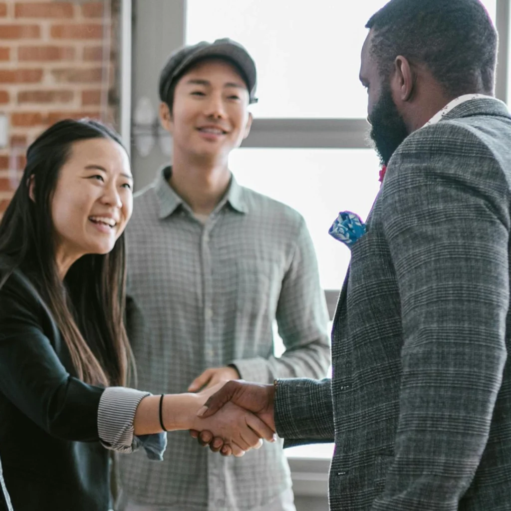 Two people shaking hands wearing fabric jackets, with a third person smiling in the background