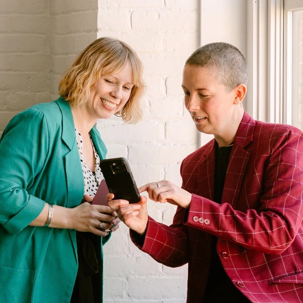 Two MQCC members looking at the Queer Business Directory on a cellphone together