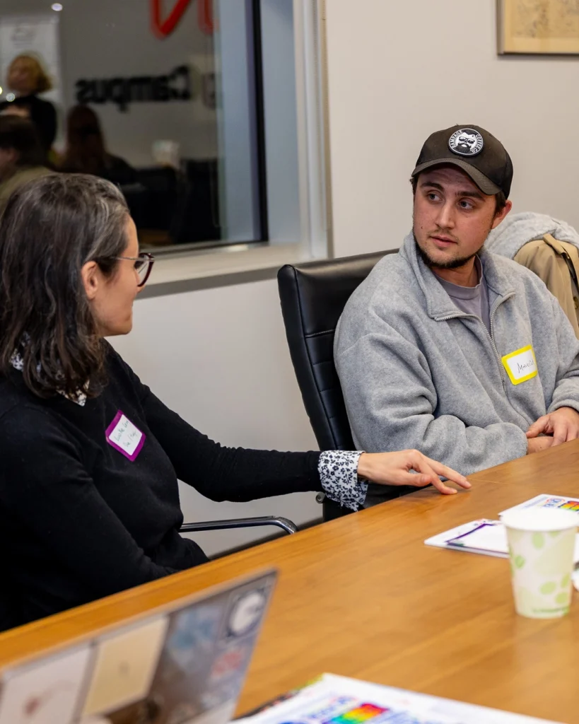 Two people sitting on black leather chairs at a wooden table in a meeting room