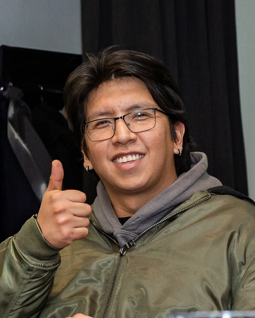 A smiling person in a grey hoodie with glasses holding up a thumbs up