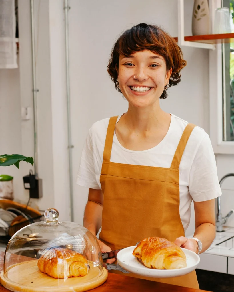 A shop owner in an apron, smiling behind a counter with pastries on it